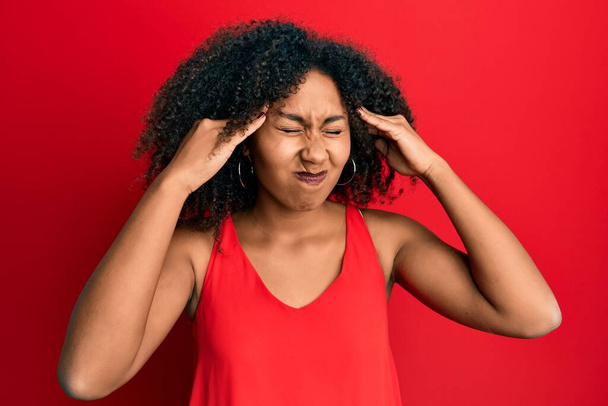 Schöne afrikanisch-amerikanische Frau mit Afro-Haaren in lässiger Kleidung mit der Hand auf dem Kopf, Kopfschmerzen wegen Stress. Migräne.  - Foto, Bild