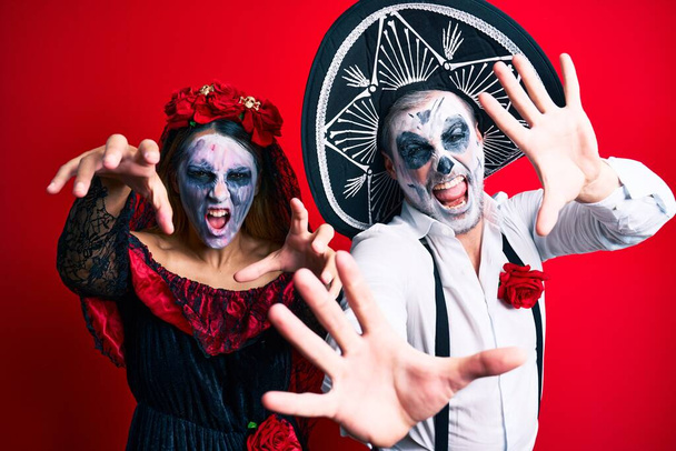 Krásný pár na sobě den mrtvých kostým gestikulace jako zombie přes izolované červené pozadí. - Fotografie, Obrázek