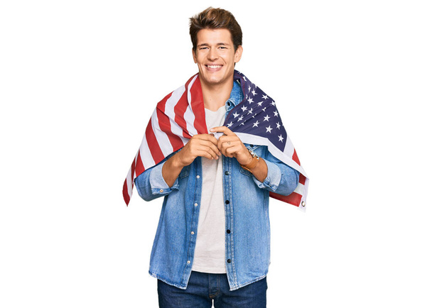 Hübscher kaukasischer Mann mit der Flagge der Vereinigten Staaten, der im Stehen positiv und glücklich aussieht und mit einem selbstbewussten Lächeln und Zähnen lächelt  - Foto, Bild