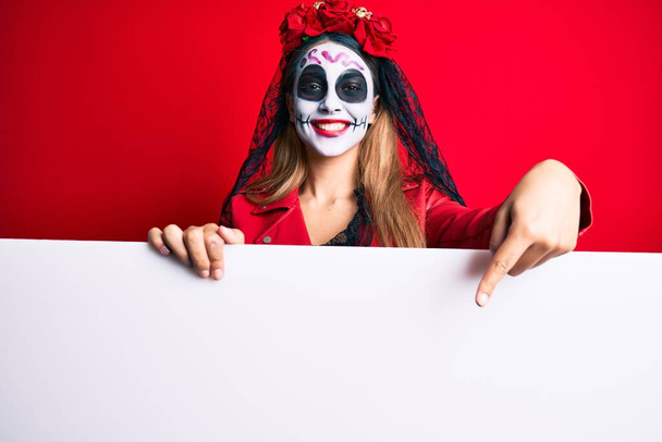 Женщина в день мертвого костюма держит пустой баннер улыбаясь счастливо указывая рукой и пальцем  - Фото, изображение