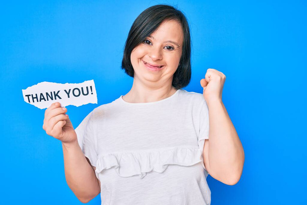 Brunette woman with down syndrome holding thank you paper screaming proud, celebrating victory and success very excited with raised arms  - Photo, Image