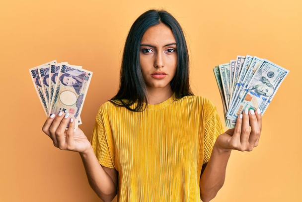 Jeune femme brune tenant un tas de dollars et de yens détendue avec une expression sérieuse sur le visage. simple et naturel regardant la caméra.  - Photo, image
