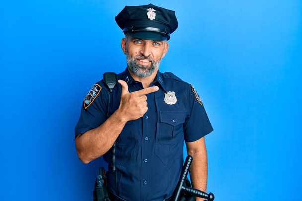 Hombre guapo de mediana edad vistiendo uniforme policial alegre con una sonrisa en la cara señalando con la mano y el dedo hacia el lado con expresión feliz y natural  - Foto, Imagen
