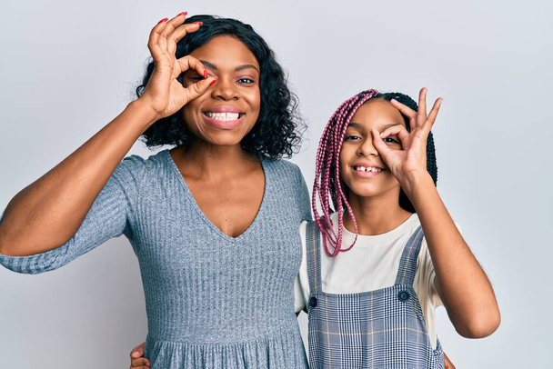 Beautiful african american mother and daughter wearing casual clothes and hugging doing ok gesture with hand smiling, eye looking through fingers with happy face.  - Fotó, kép