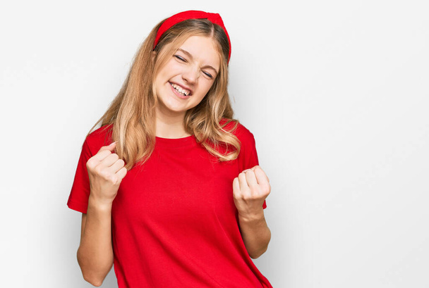 Belle jeune fille caucasienne portant t-shirt rouge décontracté excité pour le succès avec les bras levés et les yeux fermés célébrant la victoire en souriant. concept gagnant.  - Photo, image