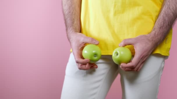 Potenz. Der Mensch hält die Äpfel in den Händen auf Höhe der Genitalien und verdreht sie. Nahaufnahme. Rosa Hintergrund. Das Konzept der Männergesundheit. - Filmmaterial, Video