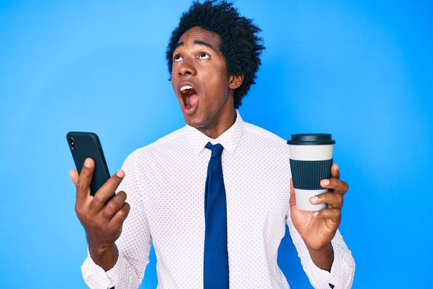 Komea afrikkalainen amerikkalainen mies afro hiukset älypuhelimella ja juo kupin kahvia vihainen ja hullu huutaa turhautunut ja raivoissaan, huutaen vihaa katselee ylös.  - Valokuva, kuva