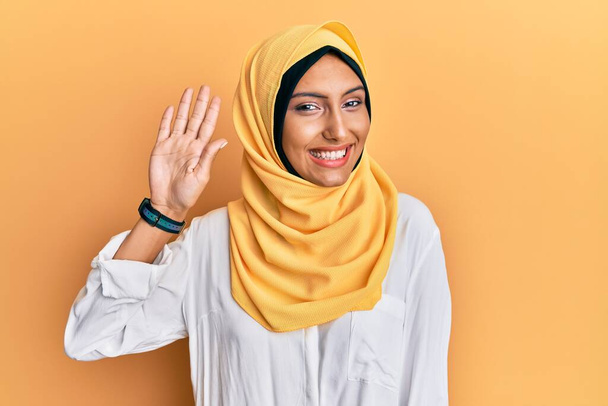 Fiatal barna arab nő visel hagyományos iszlám hidzsáb sál lemondás köszönés boldog és mosolygós, barátságos üdvözlő gesztus  - Fotó, kép