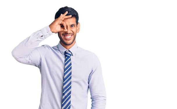 Young latin man wearing business clothes smiling happy doing ok sign with hand on eye looking through fingers  - Foto, Bild
