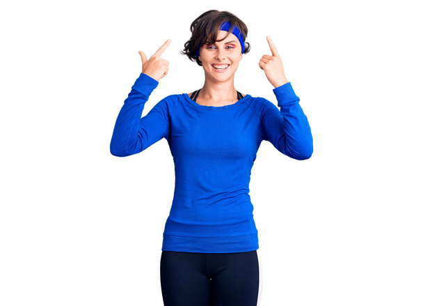 Beautiful young woman with short hair wearing training workout clothes smiling pointing to head with both hands finger, great idea or thought, good memory  - Foto, Bild