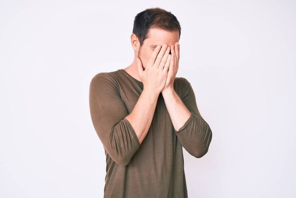 Jonge knappe man draagt casual kleding met droevige uitdrukking bedekken gezicht met handen tijdens het huilen. depressie concept.  - Foto, afbeelding