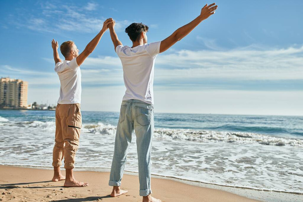 Young gay couple looking to the horizon breathing at the beach. - 写真・画像