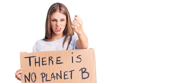 Young beautiful blonde woman holding there is no planet b banner annoyed and frustrated shouting with anger, yelling crazy with anger and hand raised  - Photo, Image