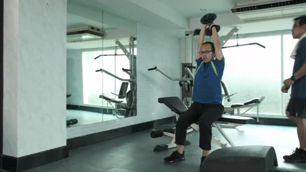 Young Asian man in sport wear practice French Press by overhead dumbbell lifting and call trainer support at GYM. sport, bodybuilding, fitness and people concept  - Footage, Video