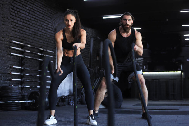 Athletic young couple with battle rope doing exercise in functional training fitness gym - Foto, Bild
