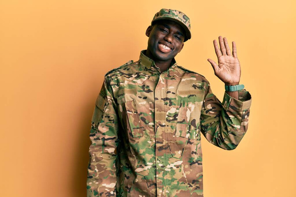 Jovem afro-americano vestindo uniforme do exército renunciando dizendo olá feliz e sorridente, gesto de boas-vindas amigável  - Foto, Imagem