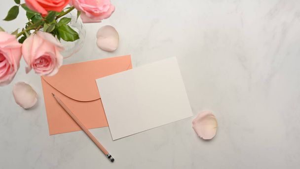Vista superior de la maqueta de tarjeta, sobre pastel, lápiz y rosa rosas flor decorada en escritorio de mármol - Foto, imagen
