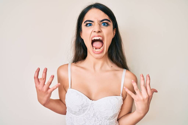 Brunette teenager girl posing elegant crazy and mad shouting and yelling with aggressive expression and arms raised. frustration concept.  - Foto, immagini