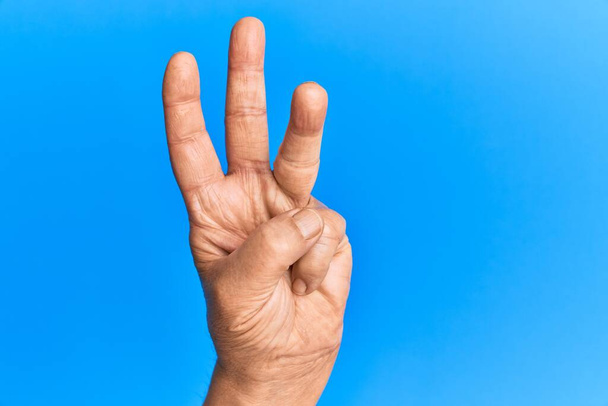 Ruka staršího hispánského muže přes modré izolované pozadí počítání číslo 3 ukazující tři prsty  - Fotografie, Obrázek