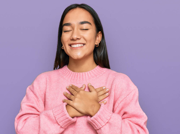 Young asian woman wearing casual winter sweater smiling with hands on chest with closed eyes and grateful gesture on face. health concept.  - Photo, Image