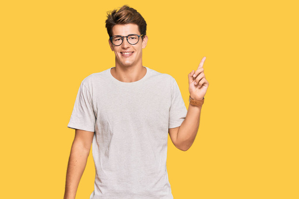 Handsome caucasian man wearing casual clothes and glasses with a big smile on face, pointing with hand finger to the side looking at the camera.  - 写真・画像