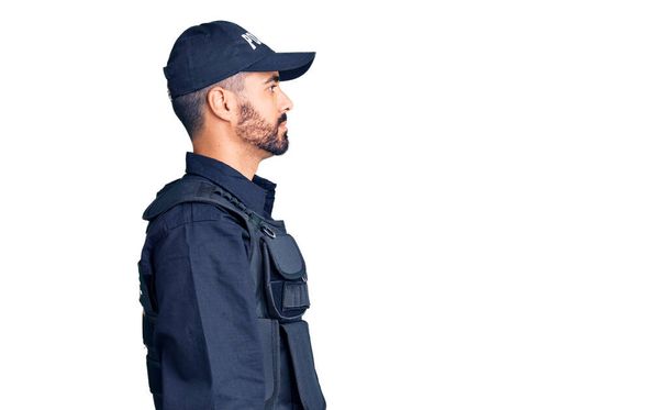 Νεαρός Ισπανός που φοράει αστυνομική στολή κοιτάζει προς τα πλάγια, χαλαρώστε προφίλ ποζάρουν με φυσικό πρόσωπο και αυτοπεποίθηση χαμόγελο.  - Φωτογραφία, εικόνα