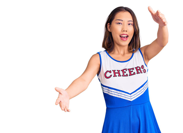 Young beautiful chinese girl wearing cheerleader uniform looking at the camera smiling with open arms for hug. cheerful expression embracing happiness.  - Fotó, kép