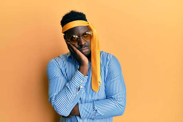 Handsome black man drunk wearing tie over head and sunglasses thinking looking tired and bored with depression problems with crossed arms.  - Photo, Image