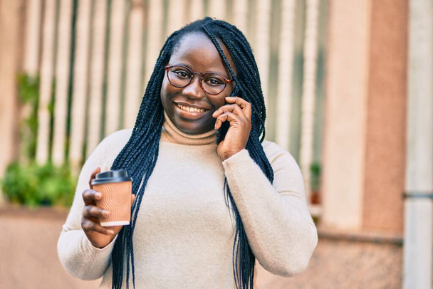 Genç Afrikalı Amerikalı kadın akıllı telefondan konuşuyor ve şehirde kahve içiyor. - Fotoğraf, Görsel