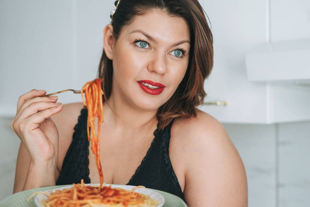 Красива щаслива чуттєва брюнетка молода жінка плюс розмір тіла позитивний зі стравою спагеті насолоджуючись її життям вдома
 - Фото, зображення