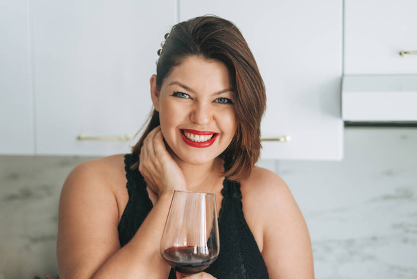 Mooie gelukkig sensuele brunette jonge vrouw plus size lichaam positief met glas rode wijn genieten van haar leven in het huis - Foto, afbeelding