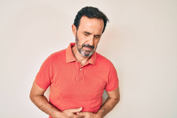 Middle age hispanic man wearing casual clothes with hand on stomach because indigestion, painful illness feeling unwell. ache concept.  - Photo, Image