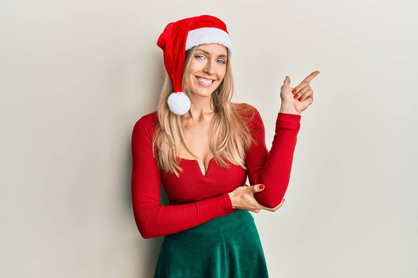 Kafkasyalı güzel bir kadın Noel kostümü ve yüzünde kocaman bir gülümsemeyle kameraya el ve parmak ile bakıyor..  - Fotoğraf, Görsel