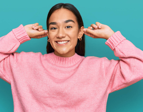 Giovane donna asiatica indossa casual maglione invernale sorridente tirando le orecchie con le dita, gesto divertente. problema di audizione  - Foto, immagini