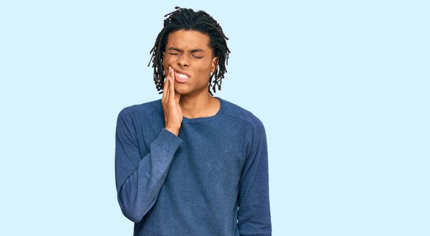 Νεαρός Αφροαμερικάνος που φοράει casual χειμωνιάτικο πουλόβερ αγγίζοντας το στόμα με το χέρι με επώδυνη έκφραση λόγω πονόδοντος ή οδοντικής πάθησης στα δόντια. οδοντίατρος  - Φωτογραφία, εικόνα