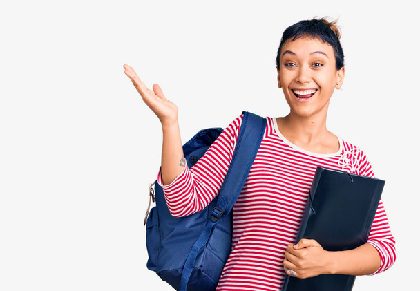 Young woman wearing student backpack holding binder celebrating victory with happy smile and winner expression with raised hands  - Φωτογραφία, εικόνα