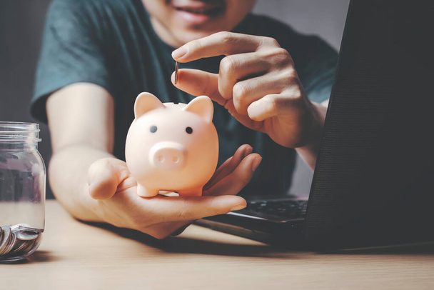 Young Asian man wearing money coin into the piggy bank Being happy with saving money and saving money. - Photo, Image