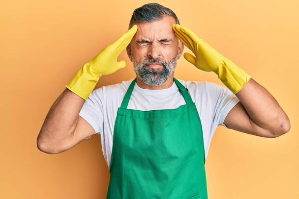 Middle age handsome man wearing cleaner apron and gloves with hand on head, headache because stress. suffering migraine.  - Fotoğraf, Görsel