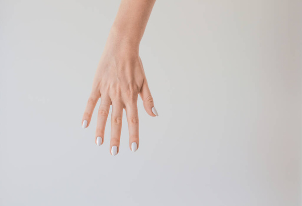  Female hand with a beautiful manicure on a background of a white wall. Delicate and healthy skin on the hands, rejuvenation of the skin of the hands, moisturizing and care. - Φωτογραφία, εικόνα