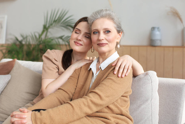 Portrait of old mother and mature daughter hugging at home. Happy senior mom and adult daughter embracing with love on sofa - Foto, immagini