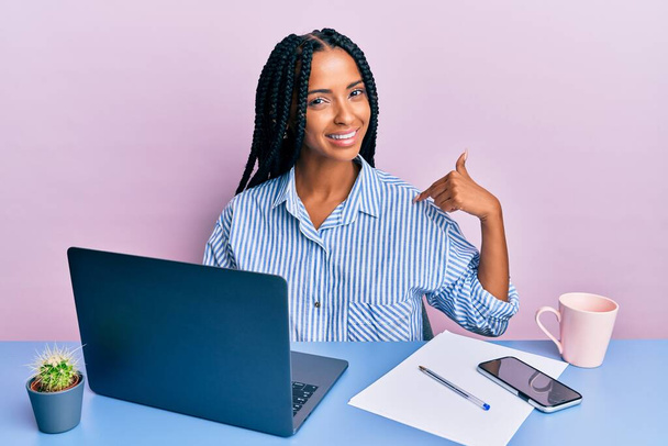 Ofiste çalışan güzel İspanyol bir kadın dizüstü bilgisayarı ile mutlu ve gururlu bir gülümsemeyi işaret ediyor.  - Fotoğraf, Görsel