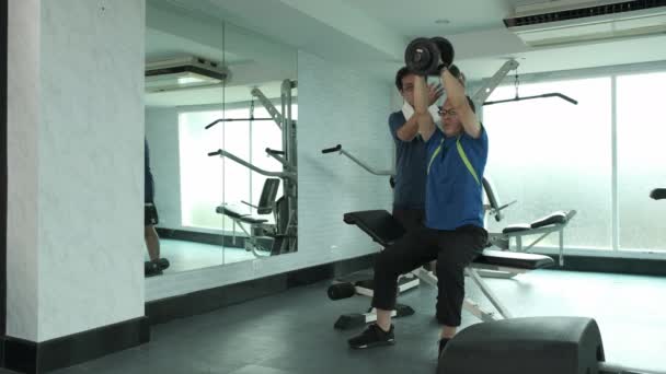 Молодой азиат в спортивной одежде практикует французскую прессу, поднимая гантели и поднимая вес на пол в GYM. спорт, бодибилдинг, фитнес и концепция людей  - Кадры, видео