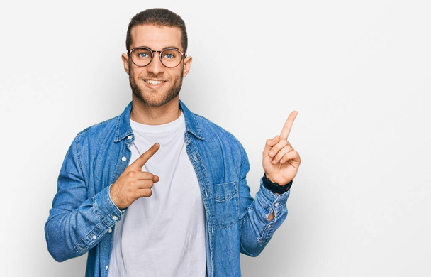 Jeune homme caucasien portant des vêtements décontractés souriant et regardant la caméra pointant avec deux mains et doigts sur le côté.  - Photo, image