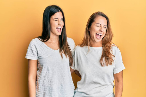 Hispanic family of mother and daughter wearing casual white tshirt winking looking at the camera with sexy expression, cheerful and happy face.  - 写真・画像