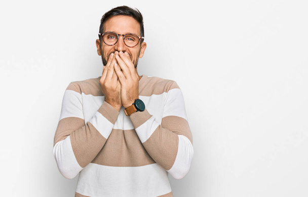 Handsome man with beard wearing casual clothes and glasses laughing and embarrassed giggle covering mouth with hands, gossip and scandal concept  - Photo, Image