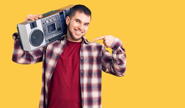 Young handsome man listening to music holding boombox pointing finger to one self smiling happy and proud  - Photo, Image