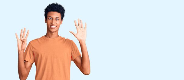 Genç, Afro-Amerikalı, günlük kıyafetler giymiş, dokuz numaralı parmaklarıyla işaret ederken, kendinden emin ve mutlu bir şekilde gülümsüyor..  - Fotoğraf, Görsel