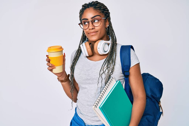 Молодая африканская американка с косичками в студенческом рюкзаке пьет кофе, улыбаясь, глядя в сторону и думая:.  - Фото, изображение
