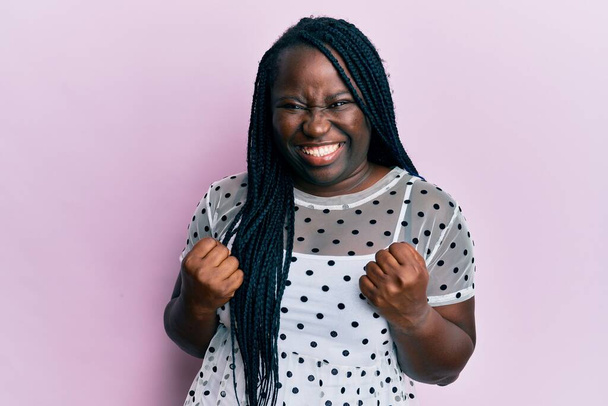 Young black woman with braids wearing casual clothes excited for success with arms raised and eyes closed celebrating victory smiling. winner concept.  - Fotoğraf, Görsel