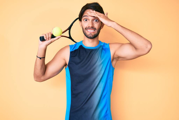 Schöner hispanischer Mann beim Tennisspielen mit Schläger und Ball gestresst und frustriert mit der Hand auf dem Kopf, überrascht und wütend  - Foto, Bild